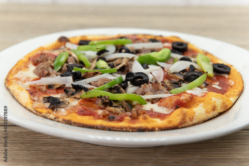 Personal sized pizza chopped vegetables and multiple meat and plenty of toppings with a crispy crust