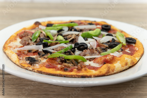 Personal sized pizza chopped vegetables and multiple meat and plenty of toppings with a crispy crust