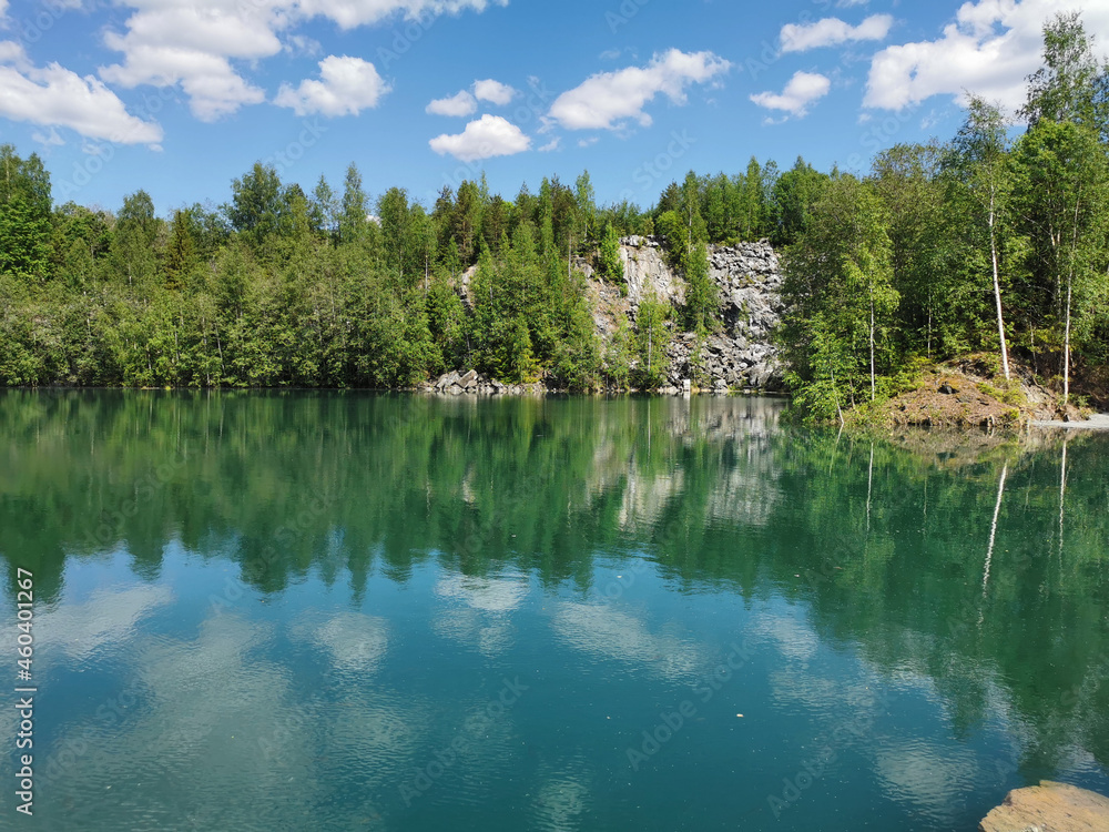 The shore of the lake Light with turquoise water, which reflects the trees and the sky with clouds, in the mountain park Ruskeala.