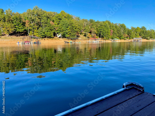 The corner of an old dock by a lake with trees and blue sky in the background..