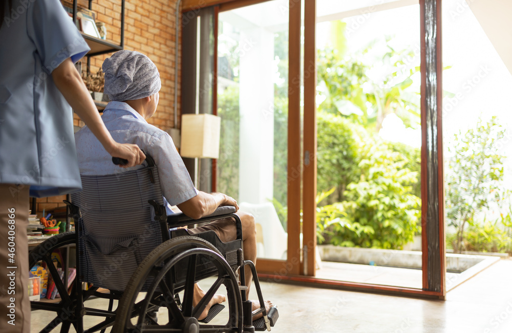 Attractive young Asian female nurse kneeling beside senior patient in wheelchair talking, smiling and cheering up in comfort at home.He survive from cancer . Attractive young Asian female nurse kneeling beside senior patient in wheelchair talking, smiling and cheering up in comfort at home.He survive from cancer .