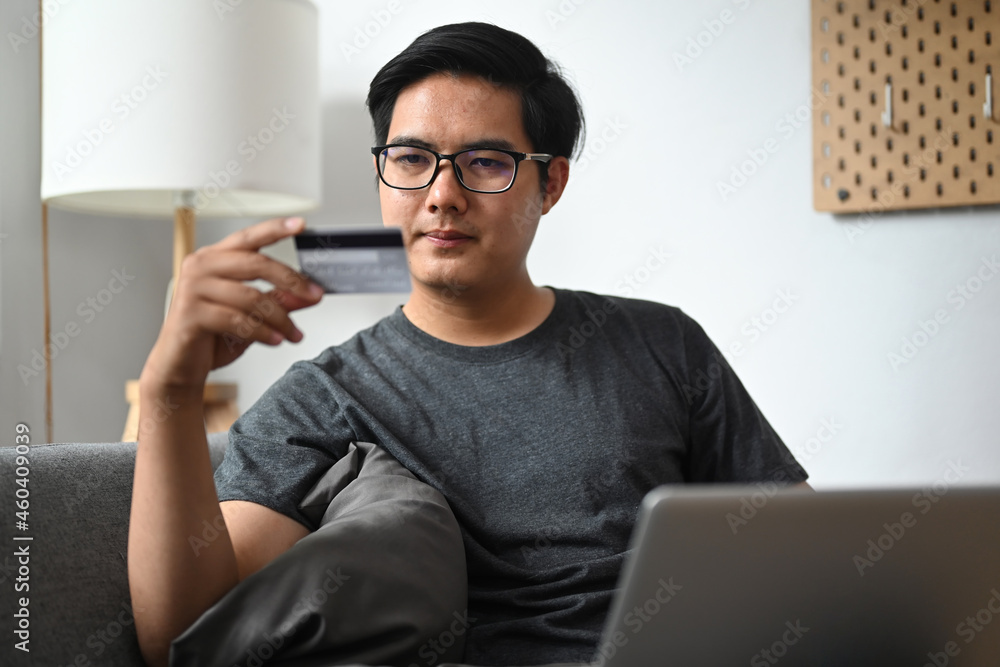 Smiling man holding credit card and shopping online with laptop computer at home. Smiling man holding credit card and shopping online with laptop computer at home.