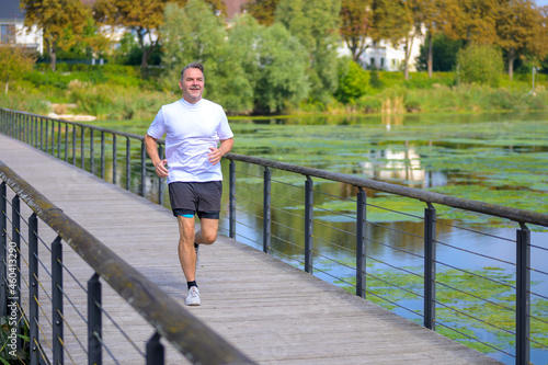 Middle-aged man jogging across a wooden footbridge © michaelheim