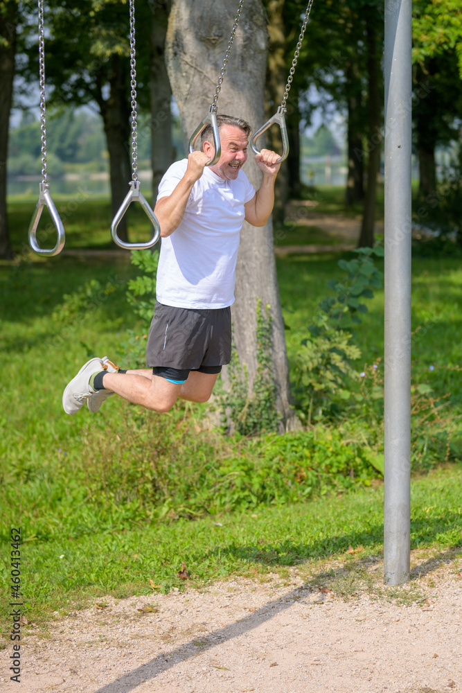Senior man working out on exercise rings in a park