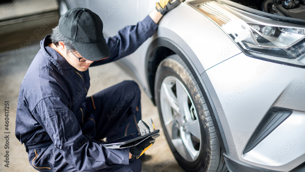 Asian auto mechanic holding digital tablet checking car wheel and tire in auto service garage. Mechanical maintenance engineer working in automotive industry. Automobile servicing and repair concept Asian auto mechanic holding digital tablet checking car wheel and tire in auto service garage. Mechanical maintenance engineer working in automotive industry. Automobile servicing and repair concept