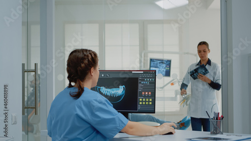 Dentistry assistant using computer with virtual teeth animation while giving x ray scan to dentist for patient examination in oral cabinet. Stomatology team with radiography and monitor