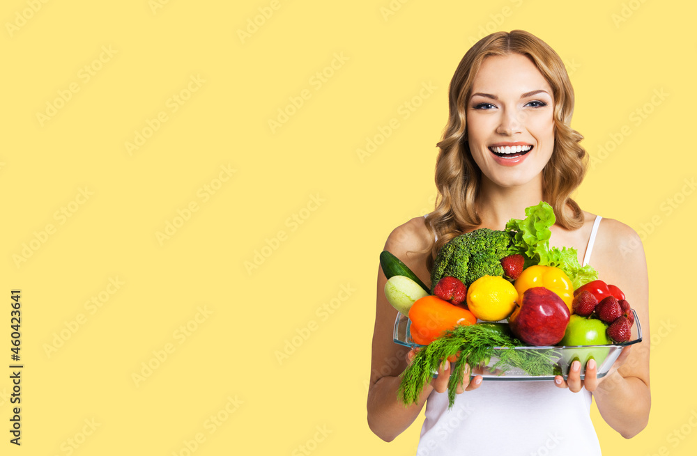 Studio portrait image of cheerful happy smiling young beautiful blond woman holding glass plate with vegetarian food. Healthy eating, dieting concept, isolated over yellow color background Studio portrait image of cheerful happy smiling young beautiful blond woman holding glass plate with vegetarian food. Healthy eating, dieting concept, isolated over yellow color background