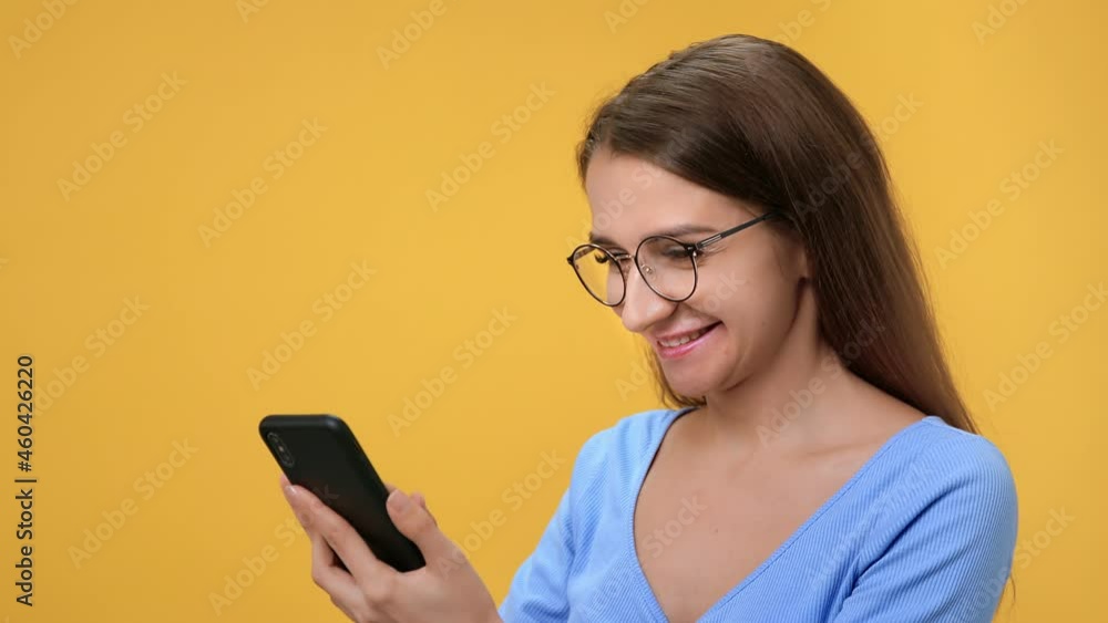 Closeup overjoyed woman in eyeglasses chatting smartphone having good news isolated on orange studio Closeup overjoyed woman in eyeglasses chatting smartphone having good news isolated on orange studio
