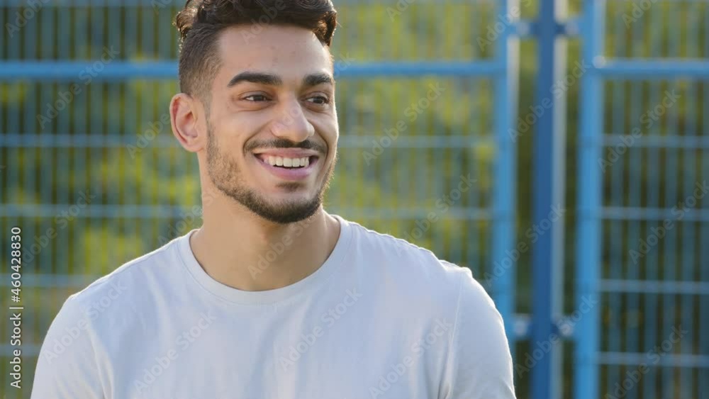 Smiling Arabic Hispanic young male soccer coach or fan in sports summer T-shirt emotionally follows match, greets players, nods approvingly, rejoices. Middle eastern indian guy supports footballers Smiling Arabic Hispanic young male soccer coach or fan in sports summer T-shirt emotionally follows match, greets players, nods approvingly, rejoices. Middle eastern indian guy supports footballers