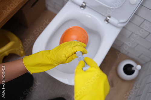Tableau sur toile Person in yellow gloves and plunger cleans toilet closeup
