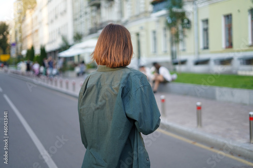 Back view of woman walking at city street at sunset wearing oversize shirt