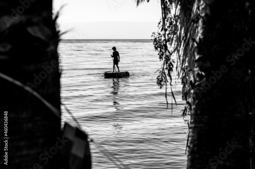 Black and white photo Silhouette of adventurous boy sail on a raft. Lake with calm water between the trees.