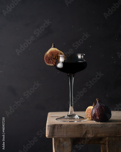 Close up of black cocktail with fresh figs and chocolate liquer on vintage wooden chair with flying drops and copy space.