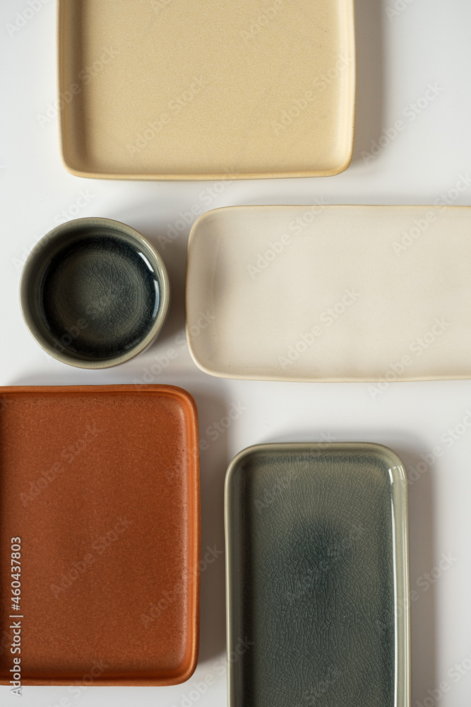 Fototapeta premium Empty blank ceramic round bowl and square plates on white background. Aesthetic minimal traditional handcrafted homemade kitchenware concept. Top view, flatlay