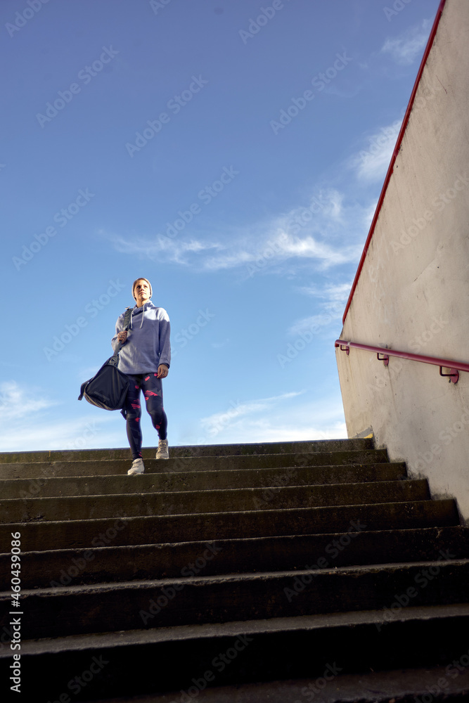 female in sportswear with a bag on her shoulder, walking down the stairs. copy space