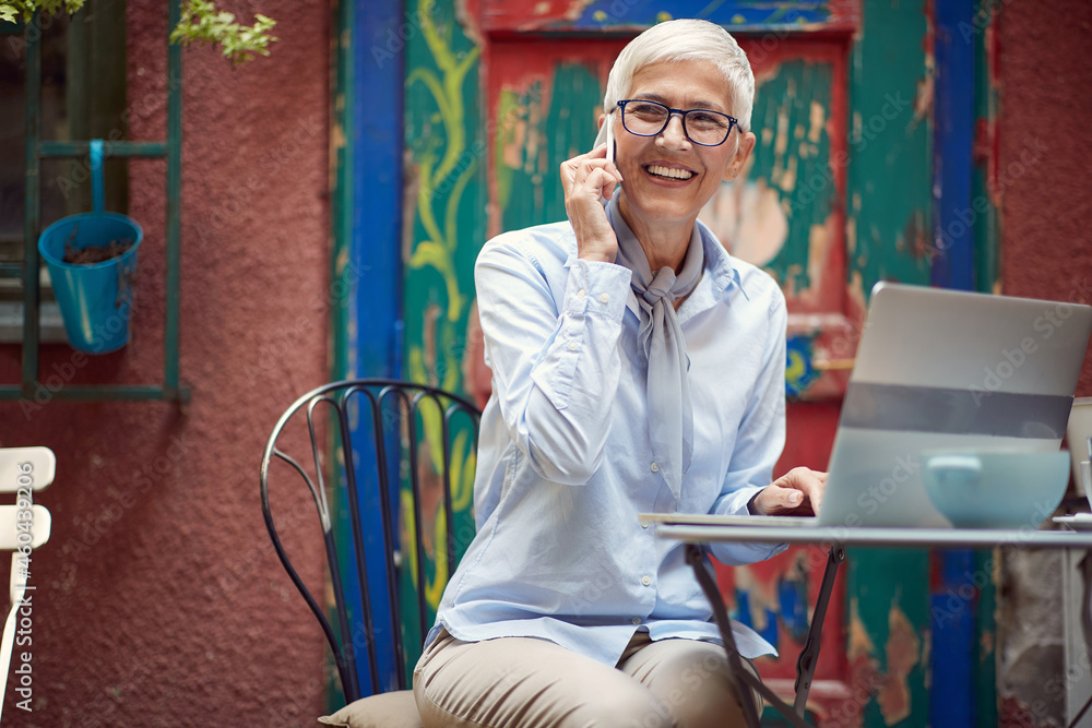 beautiful elderly female sitting at the table in the outdoor cafe, talking on her cell phone, smiling beautiful elderly female sitting at the table in the outdoor cafe, talking on her cell phone, smiling