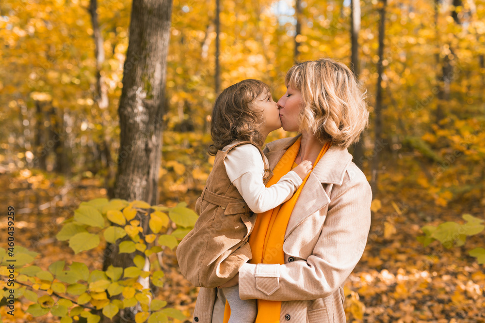 Woman with kid girl outdoors in fall. Child kissing mom. Mothers day holiday and autumn concept. Woman with kid girl outdoors in fall. Child kissing mom. Mothers day holiday and autumn concept.