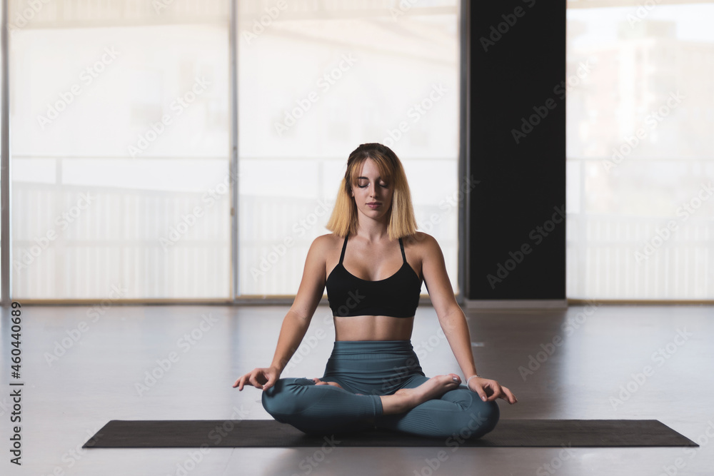 Beautiful young woman practicing yoga by the window of a gym room. Harmony, balance, meditation, relaxation, healthy lifestyle concept Beautiful young woman practicing yoga by the window of a gym room. Harmony, balance, meditation, relaxation, healthy lifestyle concept