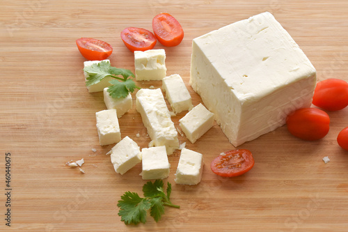 Feta cheese with cherry tomatoes and coriander on a bamboo chopping board.  The most famous Greek cheese. 