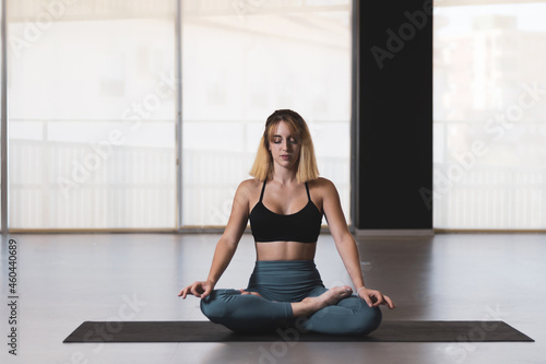 Beautiful young woman practicing yoga by the window of a gym room. Harmony, balance, meditation, relaxation, healthy lifestyle concept