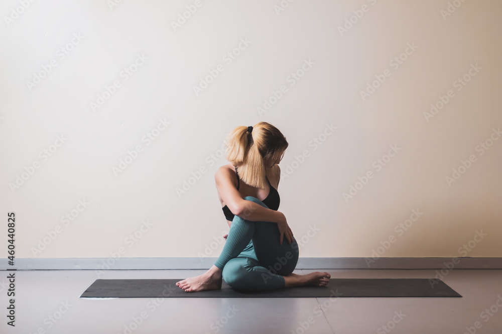 Fototapeta premium Beautiful young woman practicing yoga by the window of a gym room. Harmony, balance, meditation, relaxation, healthy lifestyle concept