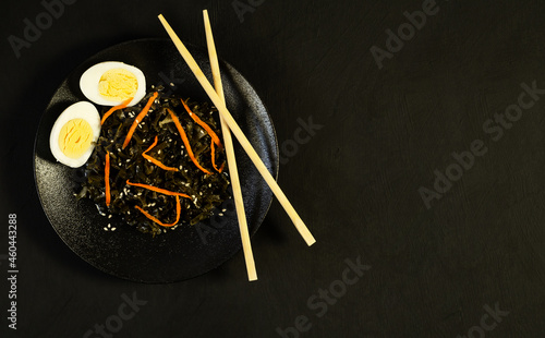 Seaweed salad with sesame seeds in a black plate with chopsticks. Black background. Japanese or Chinese kelp salad. View from above. Vegan Asian food.