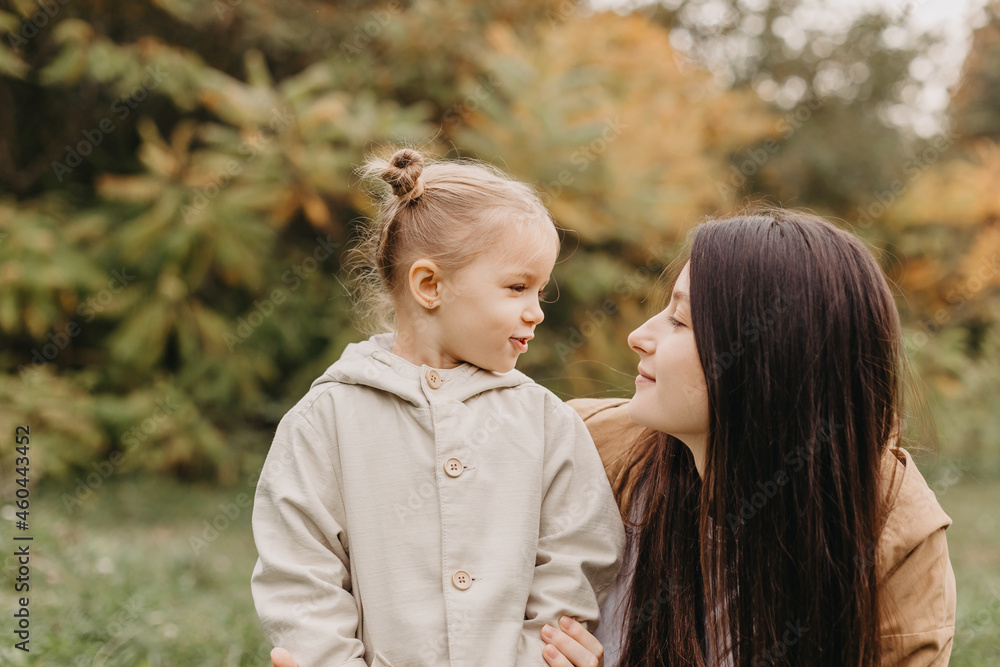 Young happy and smiling mom with her little daughter in arms hugging and kissing spending a weekend on a walk in autumn park. selective focus, noise effect, Autumnal mood Young happy and smiling mom with her little daughter in arms hugging and kissing spending a weekend on a walk in autumn park. selective focus, noise effect, Autumnal mood