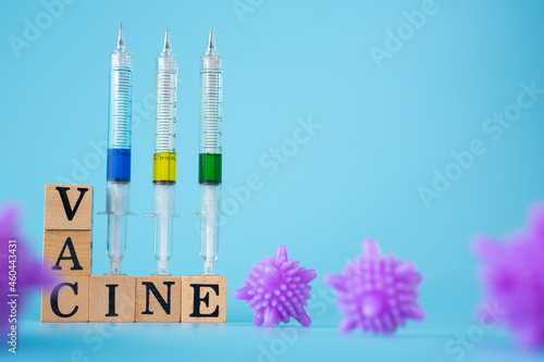 purple virus with Wooden cubes with words ''vaccine" and three syringe on blue background.
