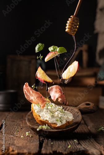 Italian crostini or bruschetta in freze motion with prosciutto,ricotta cheese,peaches,basil,thyme and pouring honey on wooden table in rustic style.Food levitation. photo