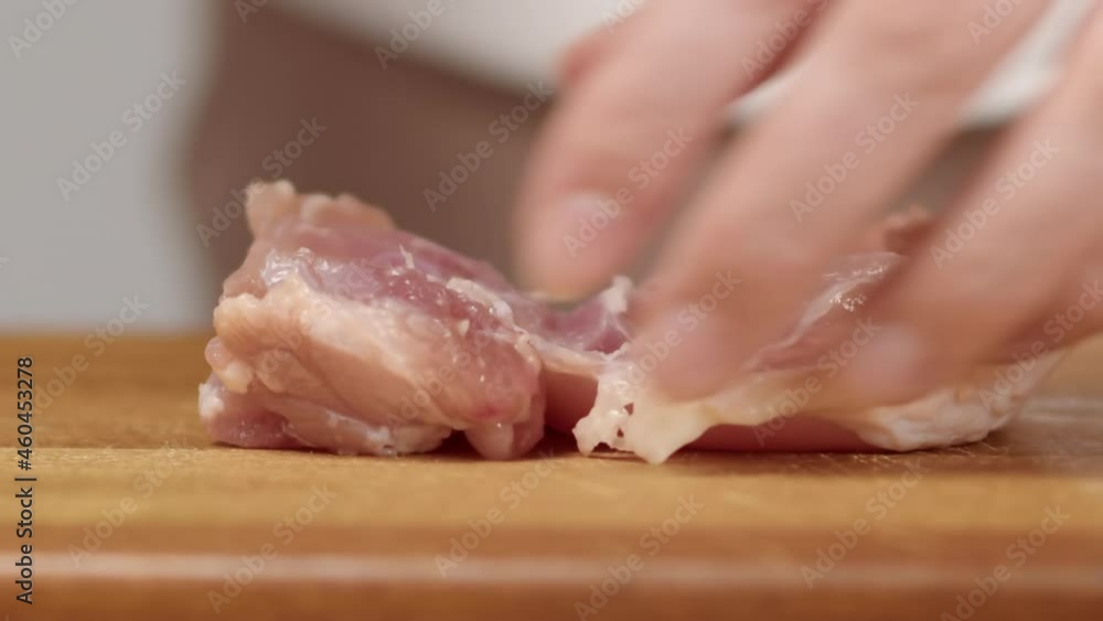 housewife takes a chicken fillet, puts it on a wooden board and cuts it into large pieces with a knife close-up slow motion housewife takes a chicken fillet, puts it on a wooden board and cuts it into large pieces with a knife close-up slow motion