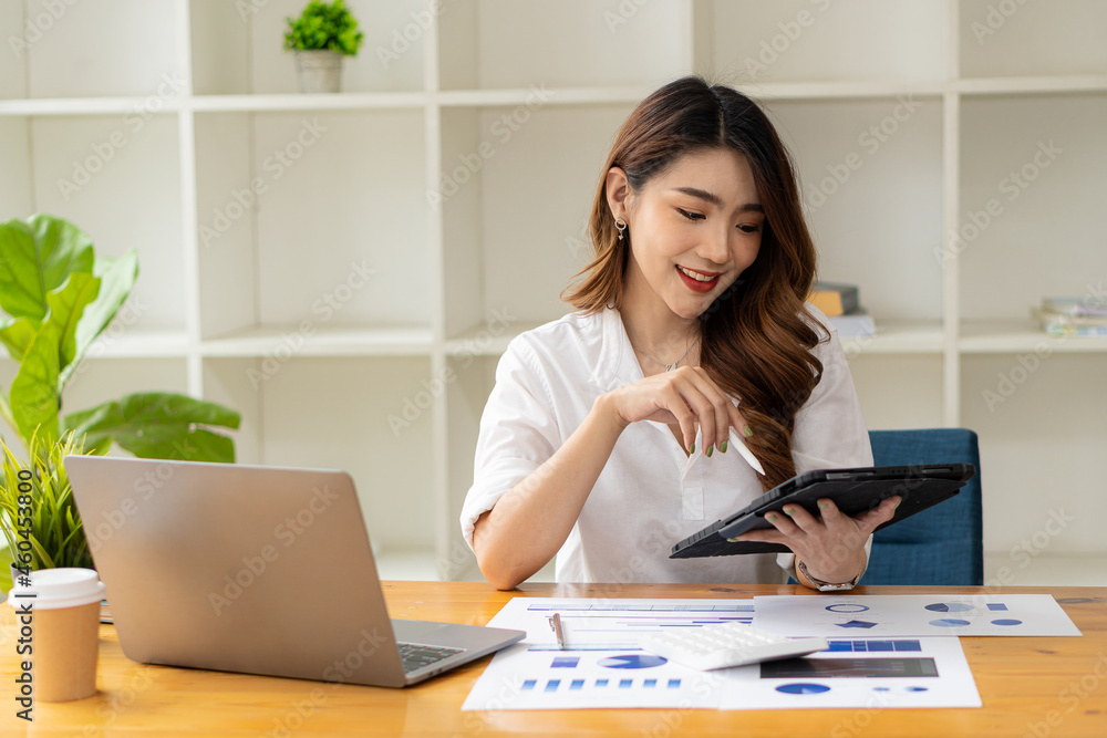 Smiling Asian businesswoman working on laptop in the office sitting at a desk in room Finance meeting to verify the accuracy of the figures in the report of the graph document. financial concept Smiling Asian businesswoman working on laptop in the office sitting at a desk in room Finance meeting to verify the accuracy of the figures in the report of the graph document. financial concept