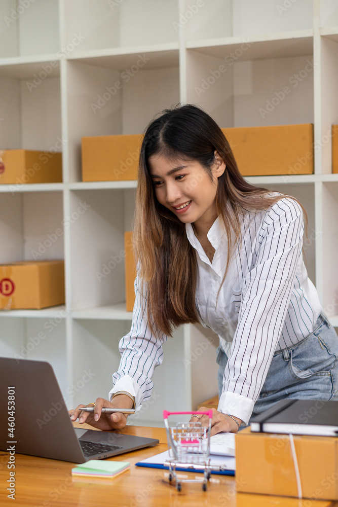 Beautiful Asian SME business owner online shopping working on laptop computer with parcel boxes on the desk at home - SME online business idea and box delivery. Beautiful Asian SME business owner online shopping working on laptop computer with parcel boxes on the desk at home - SME online business idea and box delivery.