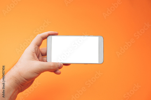 Hand holding white 3d smartphone against orange background. 3D illustration design template background. Top mobile phone message. Advertisement idea. Blank landscape copy space for ad.