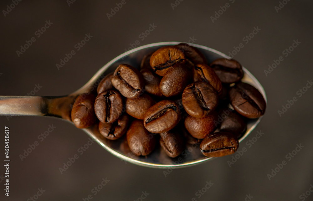 Fototapeta premium A spoon filled with roasted coffee beans on a dark background. Concept: export and import of coffee beans, coffee consumption.