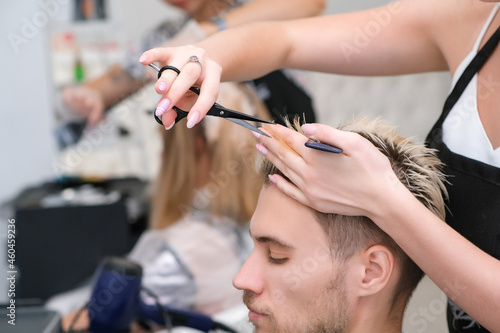 hairdresser cuts the hair of a young man with blond dyed hair with scissors in a beauty salon.