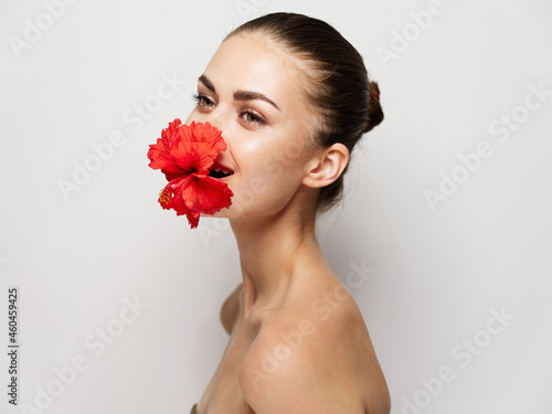 attractive woman naked shoulders red flower in mouth cropped view