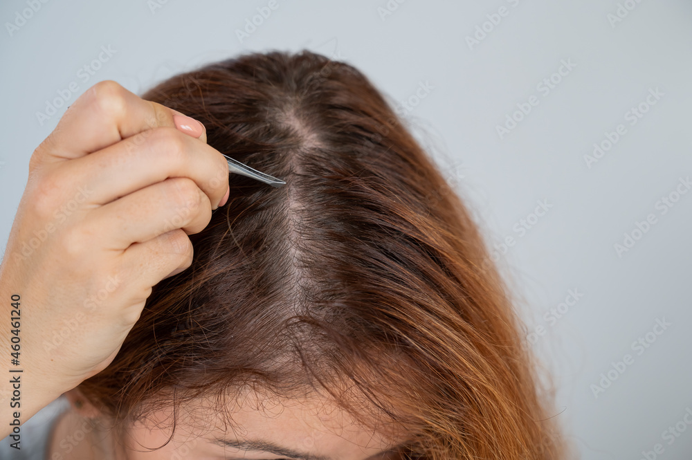Caucasian woman finds gray hair and removes it with tweezers. Signs of aging. Caucasian woman finds gray hair and removes it with tweezers. Signs of aging.