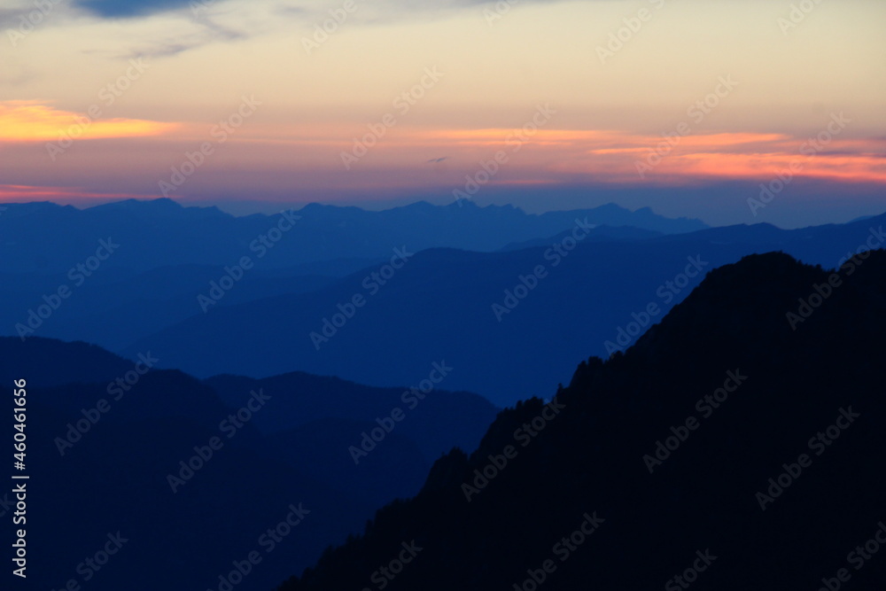 Top view of the silhouettes of blue high-mountain ranges at sunset at dusk in Altai on the Kara-Turek pass in summer, beautiful sky with clouds and pink sunlight