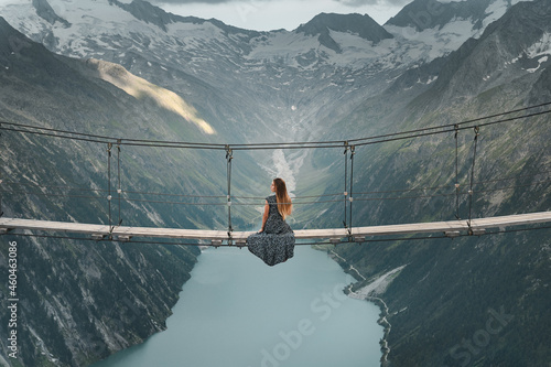 Young woman in beautiful dress sitting on a suspended bridge near Olperer Hütte photo