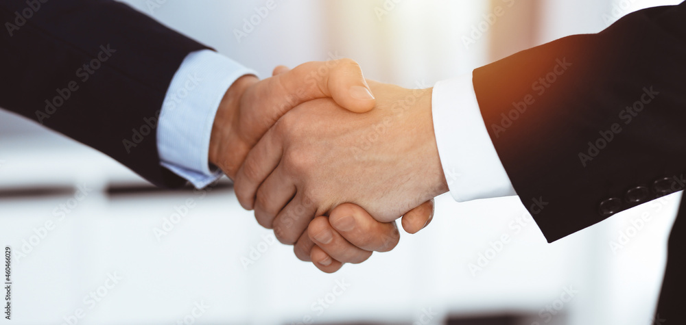 Business people shaking hands after contract signing in sunny modern office. Teamwork and handshake concept