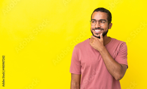Young latin man isolated on yellow background looking to the side and smiling