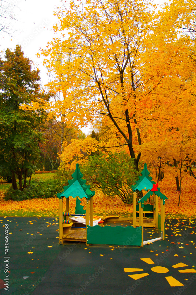 Children's playground in bright colors in a park with yellowed trees.