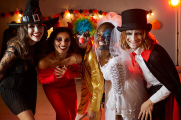 Adult friends having fun at Halloween party. Group shot of happy people dressed up in spooky costumes of witch, devil, clown, corpse bride and vampire standing together, looking at camera and smiling