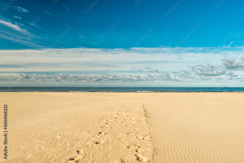 Large, empty beach with fine white sand over blue sky in in Liepaja, Latvia. Footprints in the sand leading to to sea. Latvian landscape captured in a sunny autumn day. Popular holiday destination. 