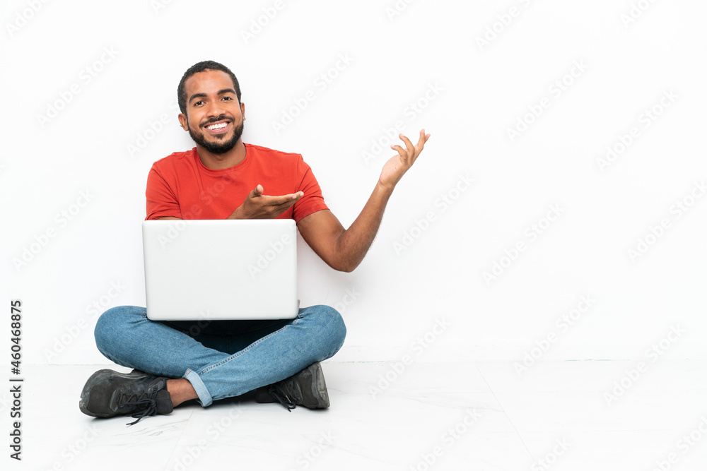 Young Ecuadorian man with a laptop sitting on the floor isolated on white background extending hands to the side for inviting to come Young Ecuadorian man with a laptop sitting on the floor isolated on white background extending hands to the side for inviting to come