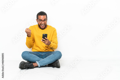 Young Ecuadorian man sitting on the floor isolated on white wall surprised and sending a message