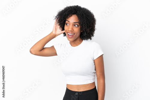 Young African American woman isolated on white background listening to something by putting hand on the ear © luismolinero