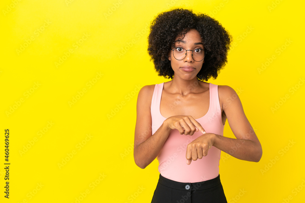 Young African American woman isolated on yellow background making the gesture of being late