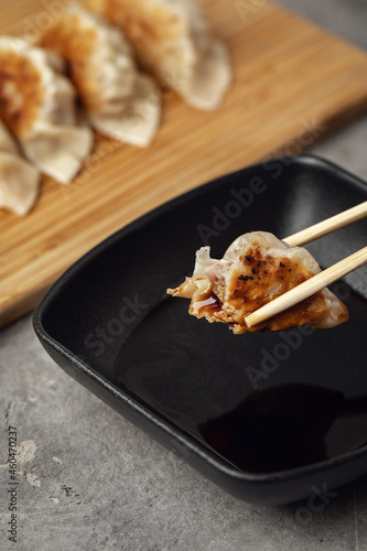 Gyoza or dumplings snack with soy sauce on wood board and grey clay background. Using chopsticks
