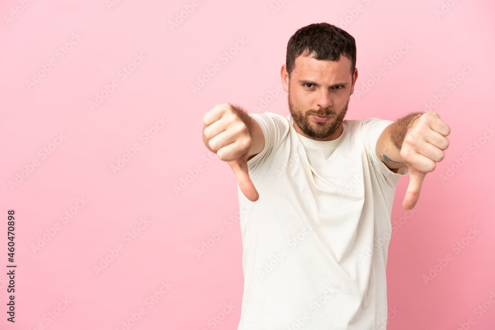 Young Brazilian man isolated on pink background showing thumb down with two hands Young Brazilian man isolated on pink background showing thumb down with two hands